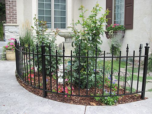 A black wrought iron fence surrounds a garden in front of a house.