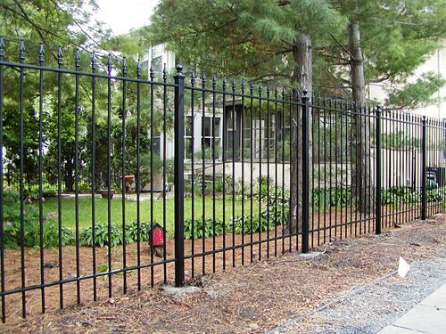 A black wrought iron fence surrounds a lush green yard.