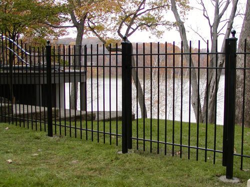 A black fence surrounds a grassy area with a lake in the background