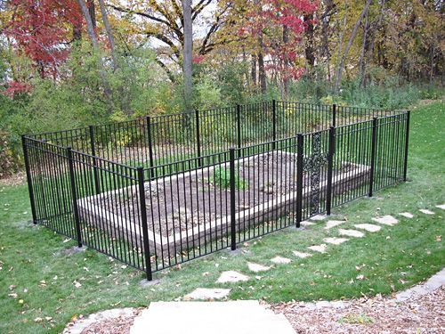 A wrought iron fence surrounds a garden in a backyard.