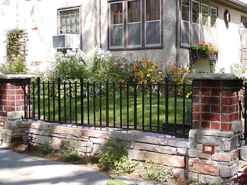 A wrought iron fence surrounds a brick wall in front of a house