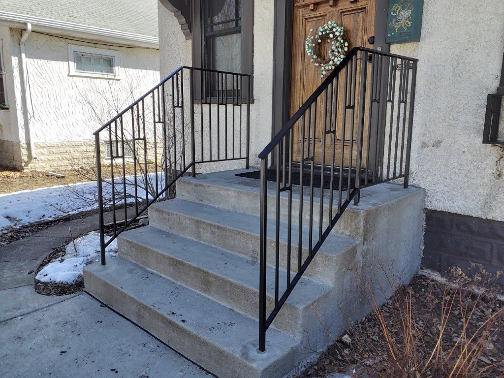 Black metal railing on concrete steps leading to a front door with a wreath.