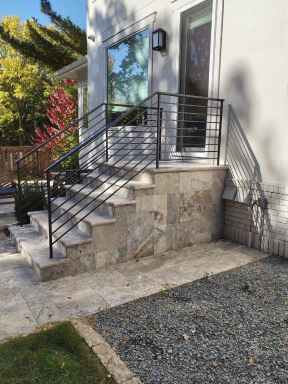 Stone steps with black metal railing leading up to a white house with large windows.