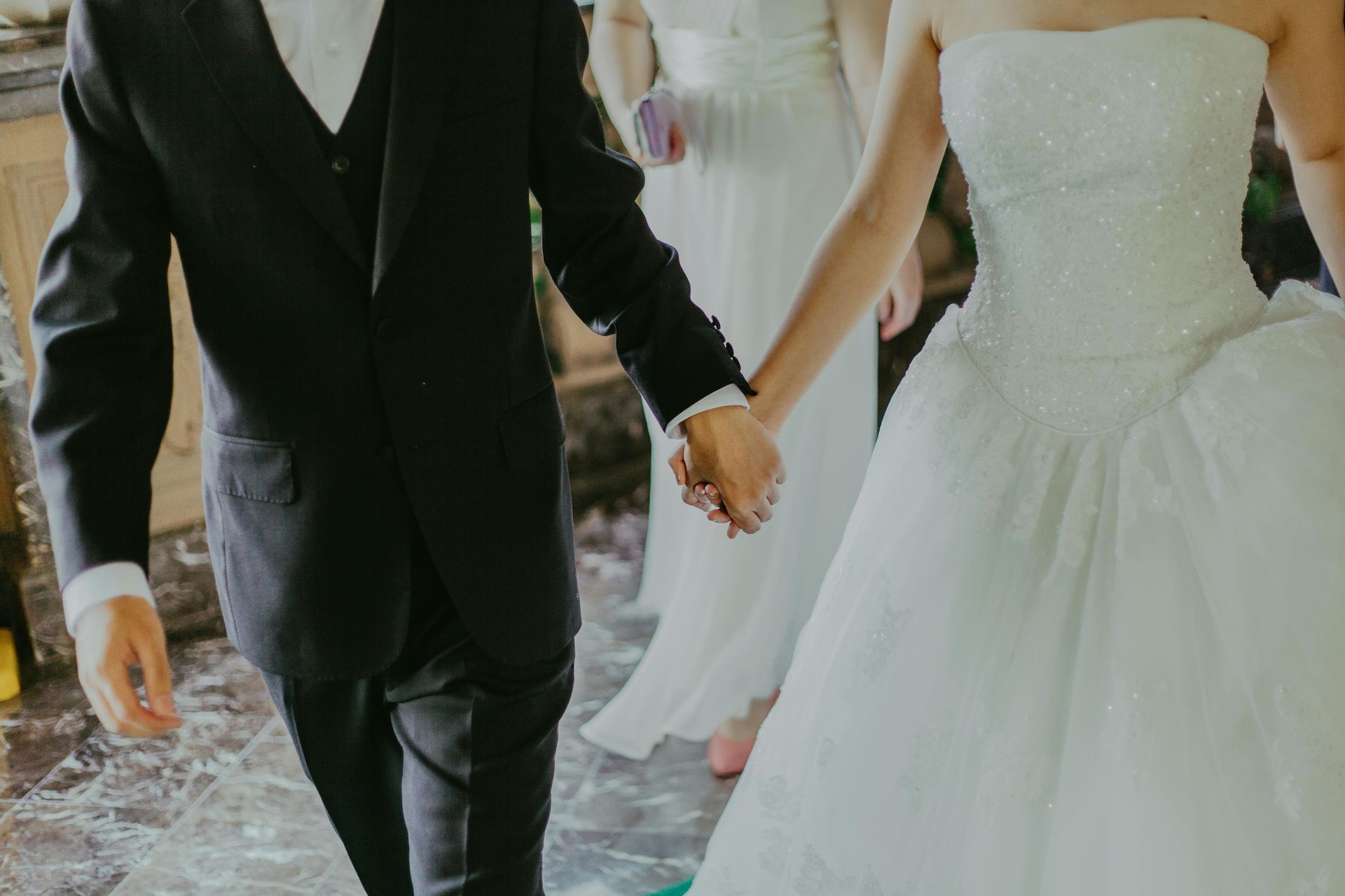 Couple in wedding attire holding hands, walking together. Bride in white gown, groom in black suit.