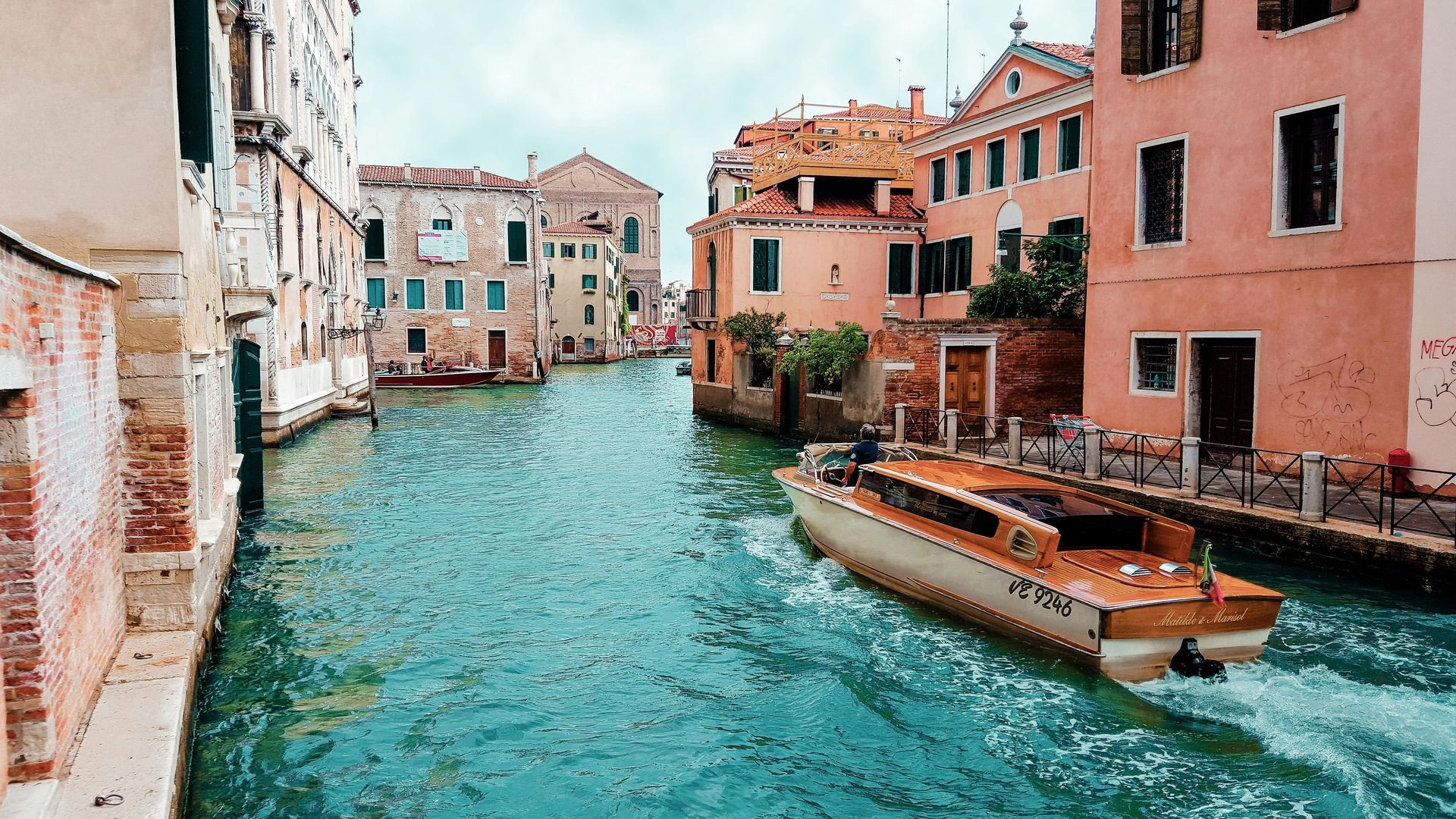 Venice canal with a boat, surrounded by colorful buildings under a cloudy sky.