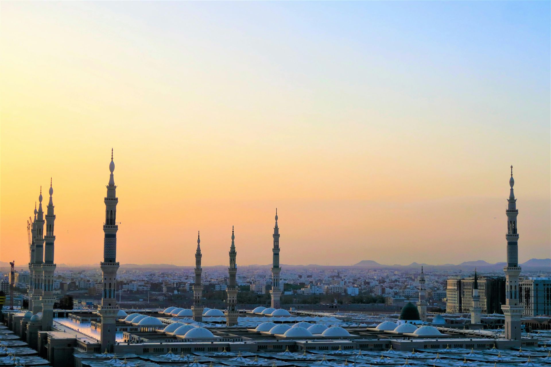 Mosque at sunset with numerous minarets and city skyline in the background.