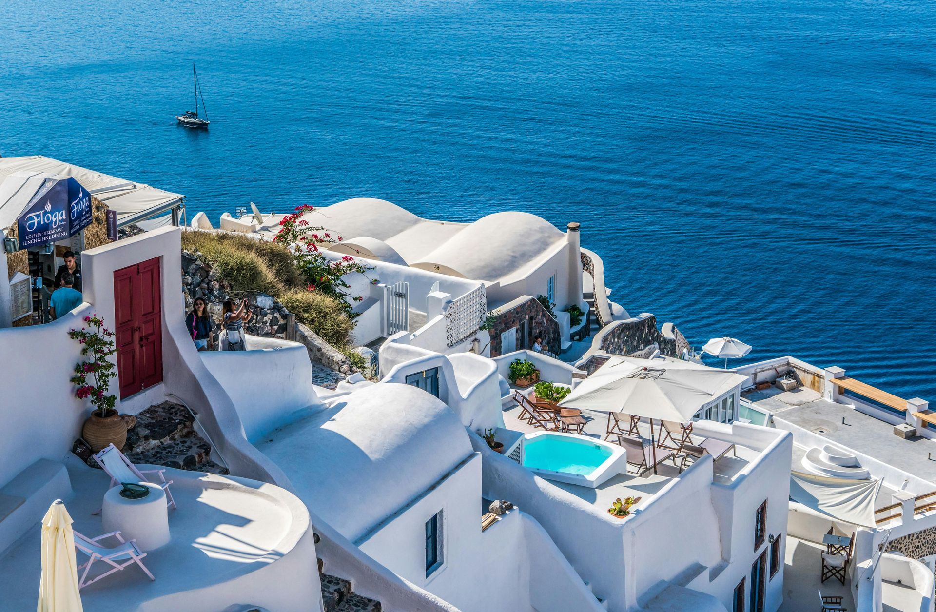Whitewashed buildings with domed roofs and blue accents on a cliffside overlooking the Aegean Sea.