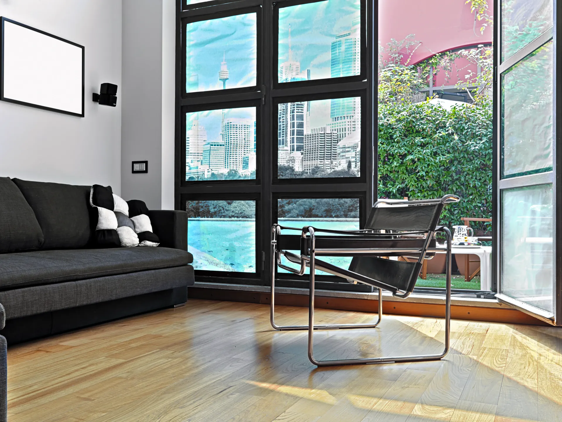 Modern living room with black sofa, large windows, glass chair, and sunlight on wood floors