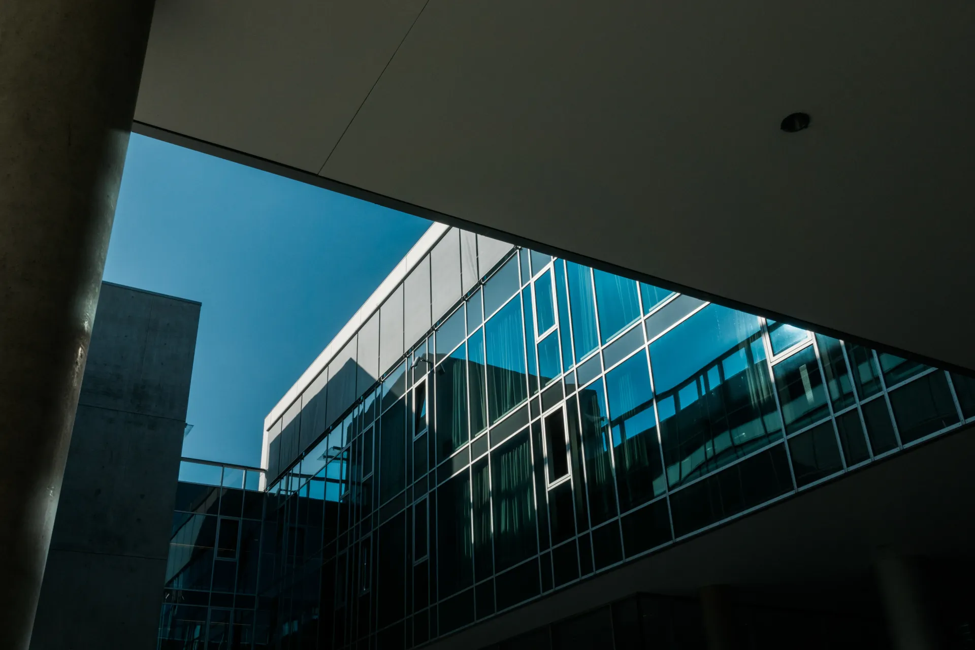 Glass office building reflected in a modern courtyard under a blue sky
