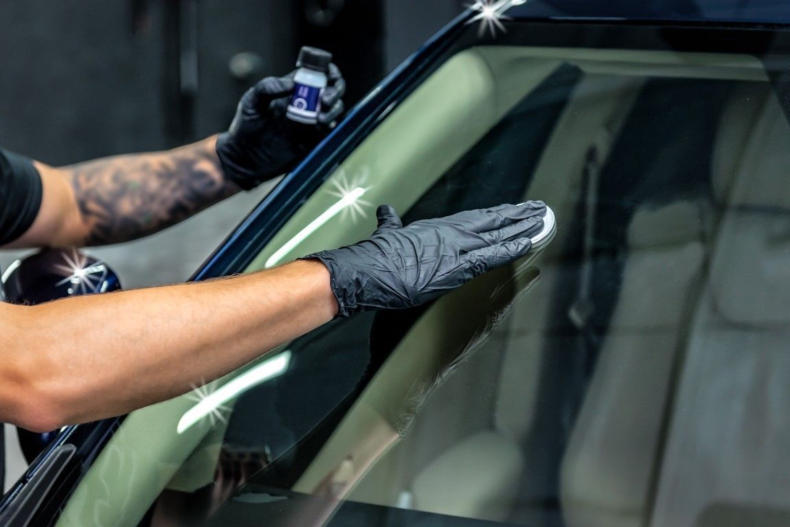 Gloved hands cleaning a car windshield with a spray bottle and cloth