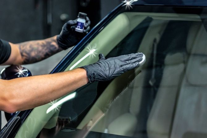 Gloved hands cleaning a car windshield with a spray bottle and cloth