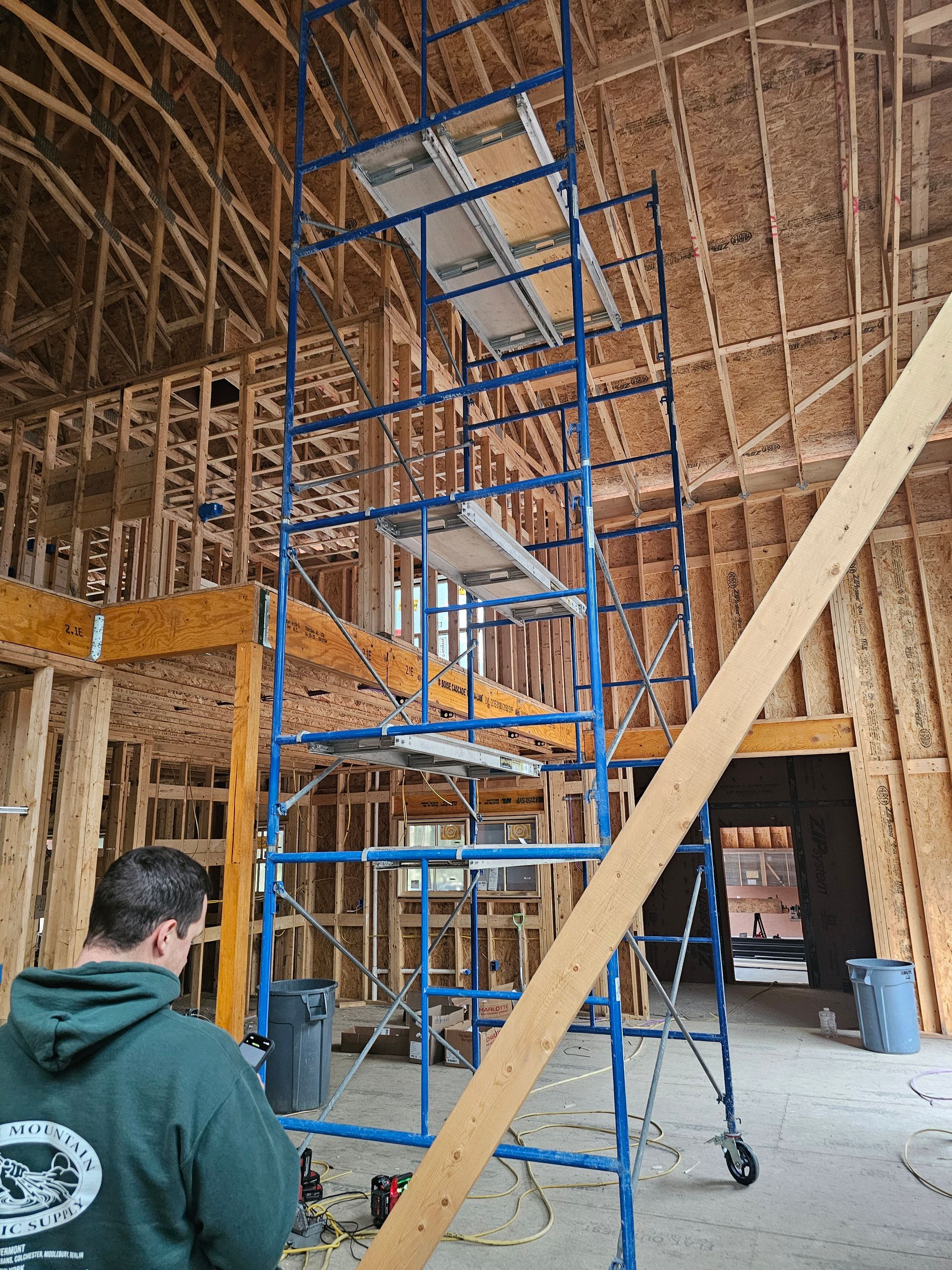 Man in green shirt near tall blue scaffold inside building under construction.