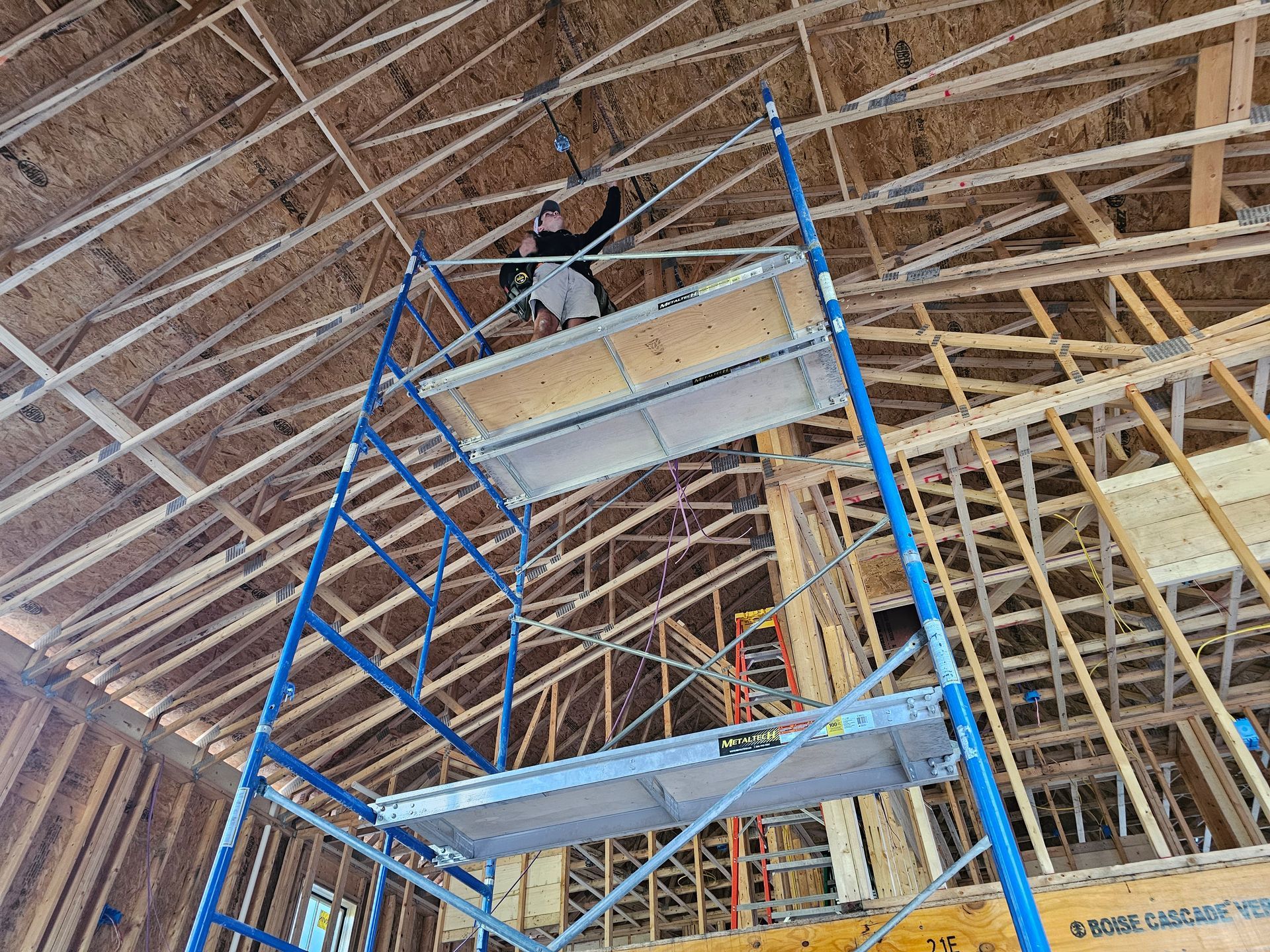 Person on scaffolding in a building under construction, working on ceiling wiring.