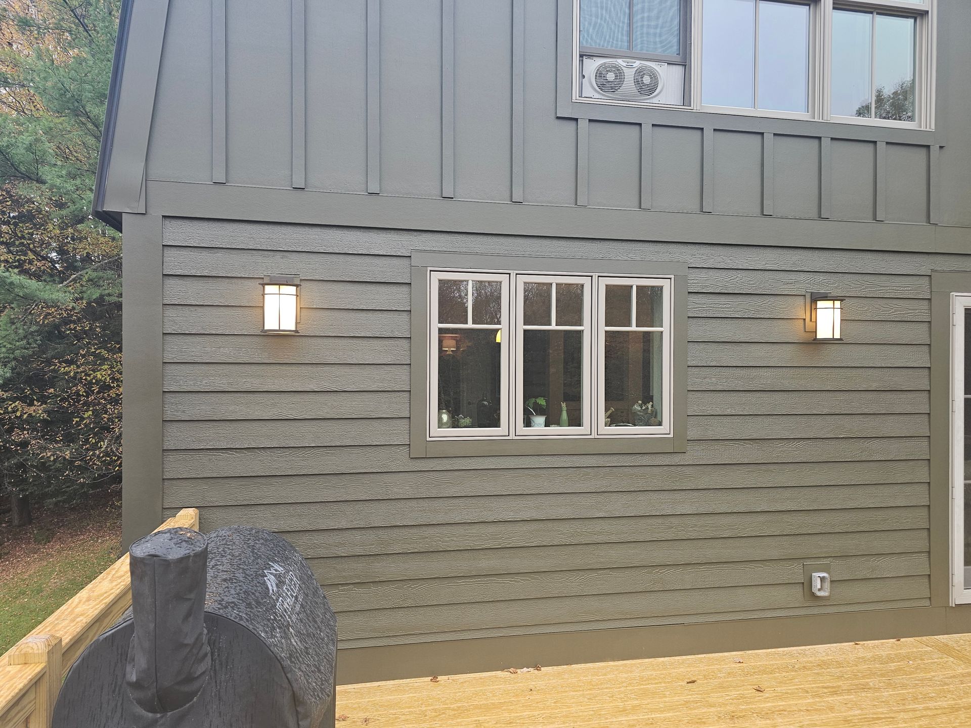 Gray siding on a building with two windows and sconces. Outdoor patio with a decorative object.
