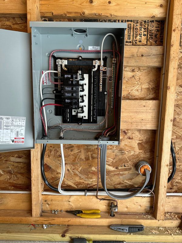Electrical panel with wires and circuit breakers installed on a wood frame wall.