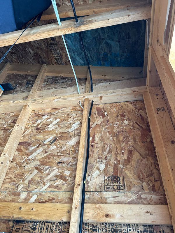 Interior view of a wooden framed wall with black wires running along it. Blue material in the upper right.