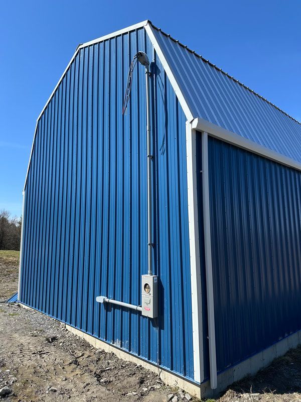 Blue metal barn with white trim and electrical components on the side.