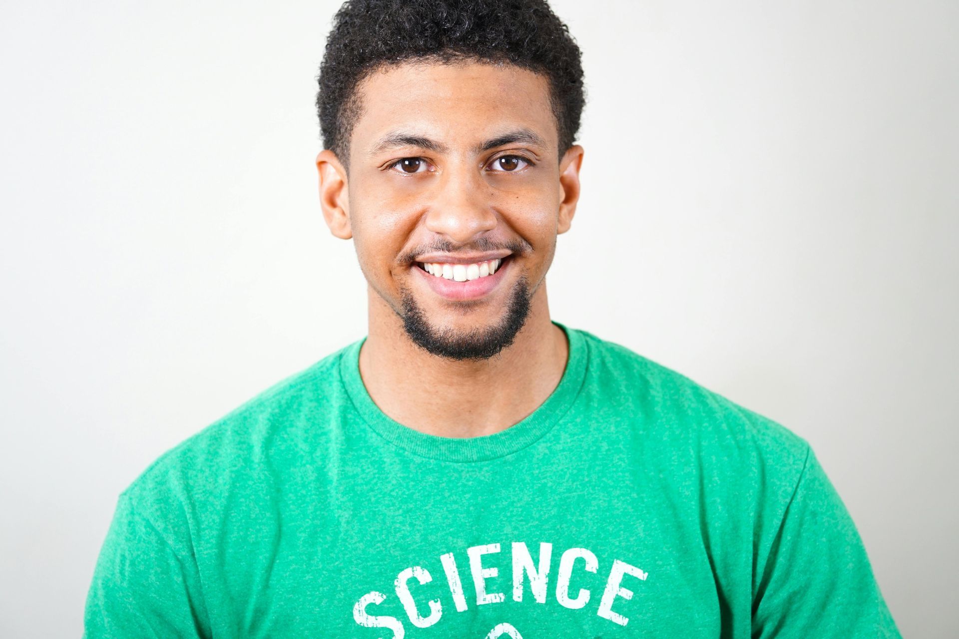Man with a short beard smiles, wearing a green shirt with