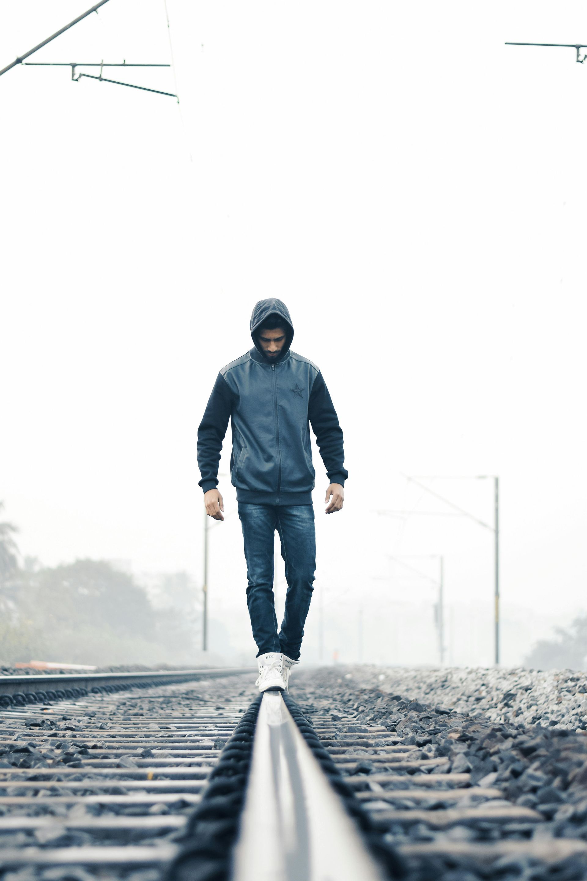 Person in a hooded jacket walks on railroad tracks in a foggy outdoor setting.