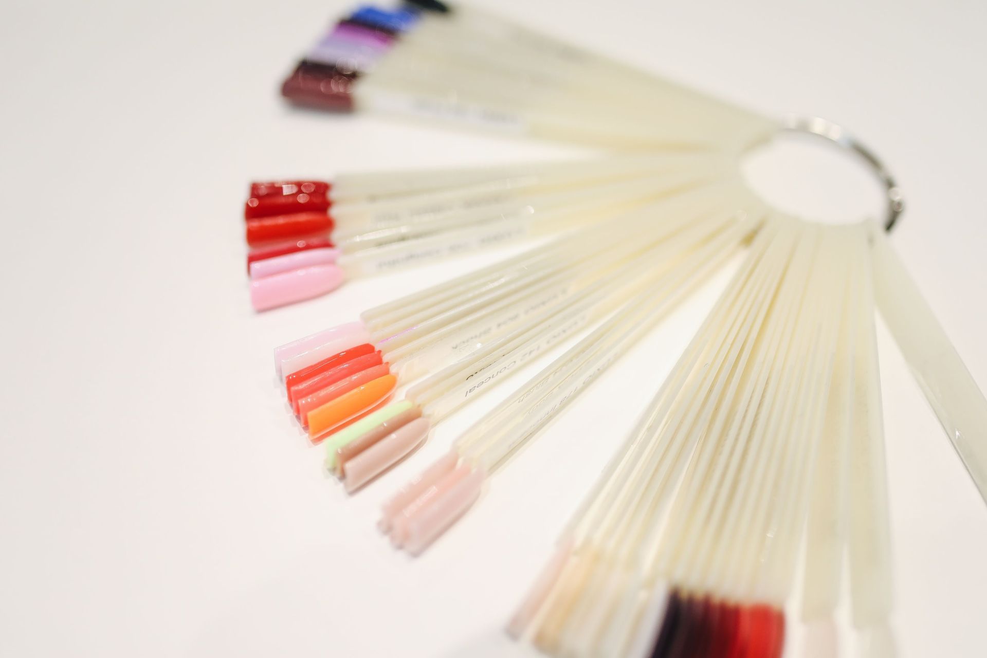 Fan of nail color swatches in pink, red, and nude shades on a white background
