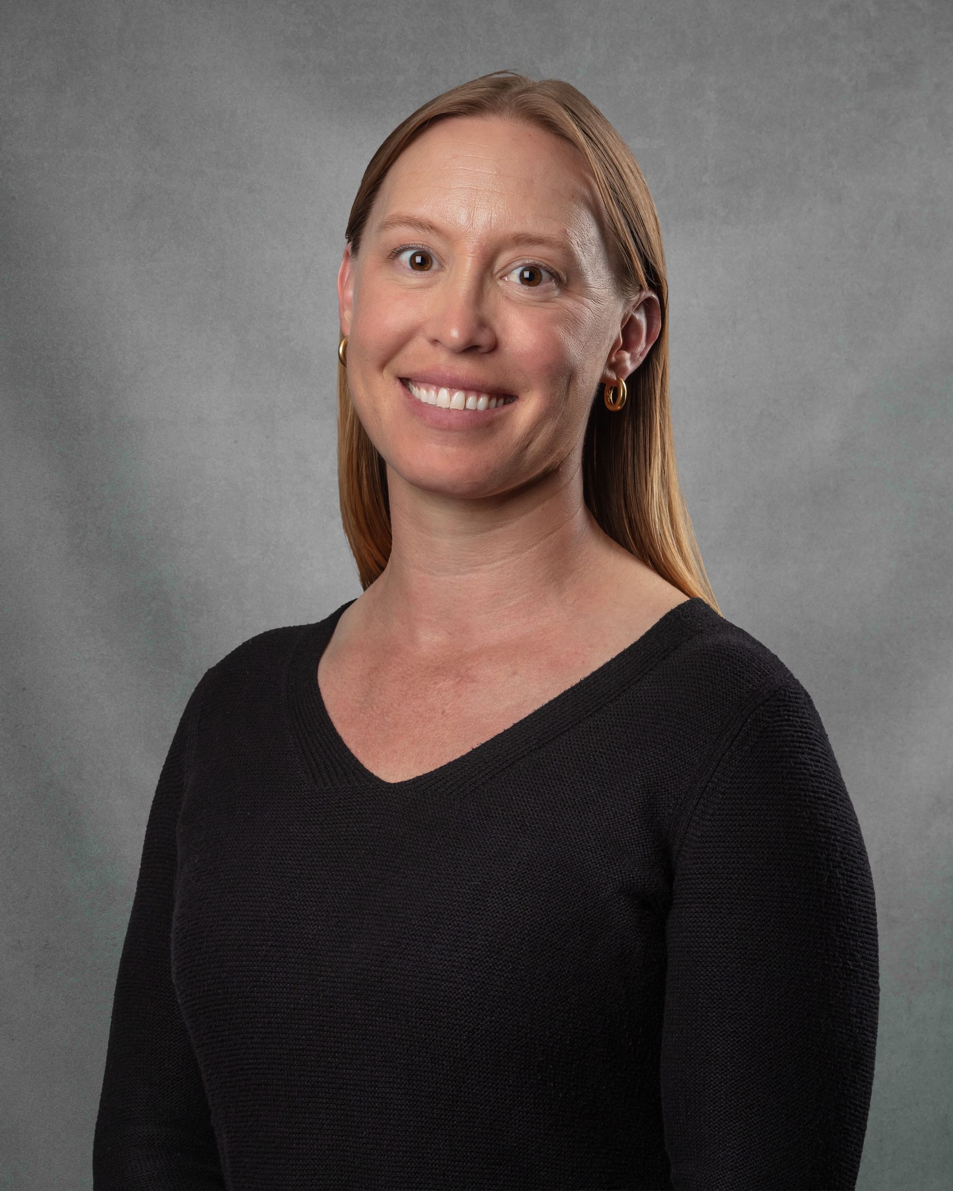 A woman in blue scrubs is smiling.