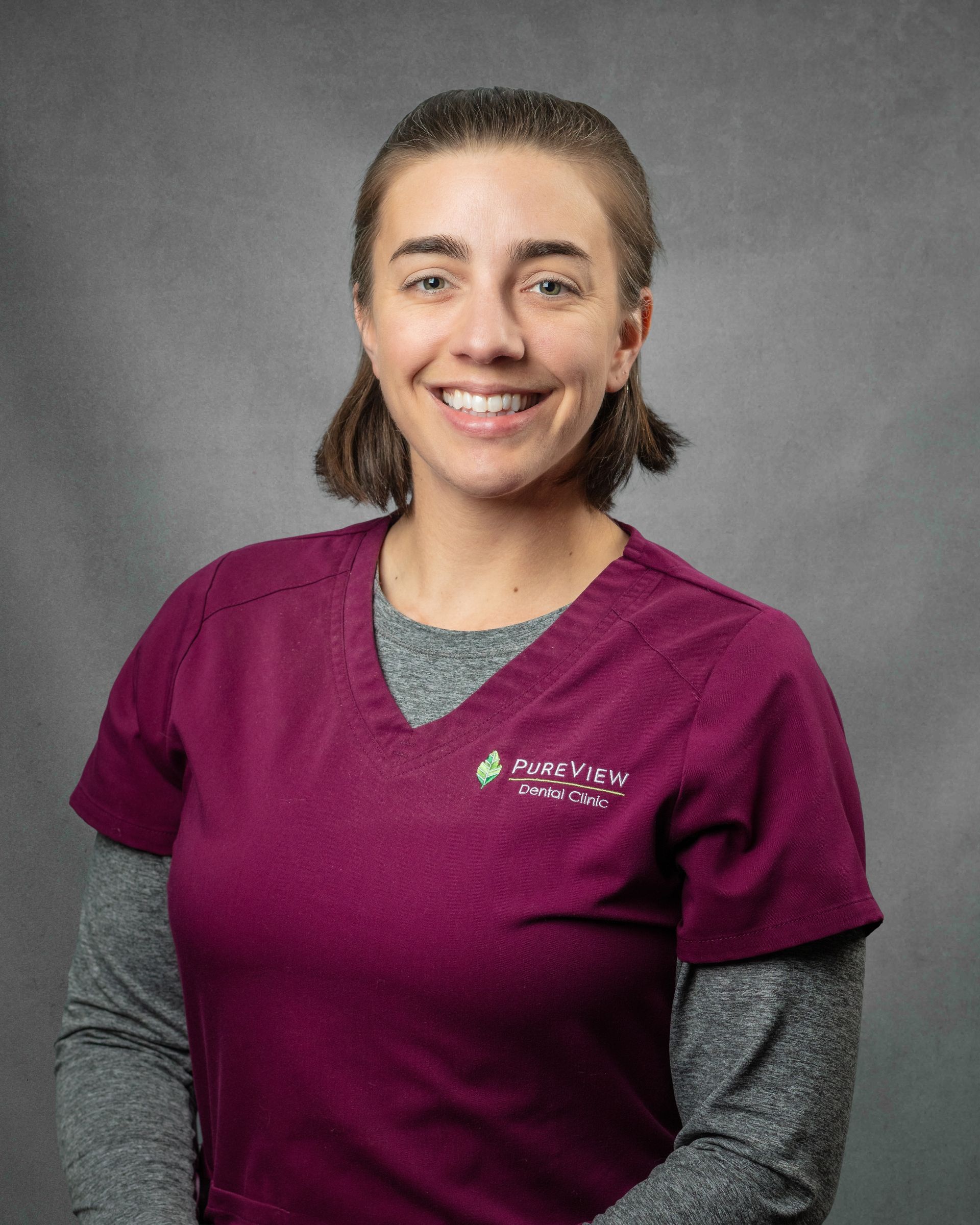 A woman in purple scrubs is smiling.