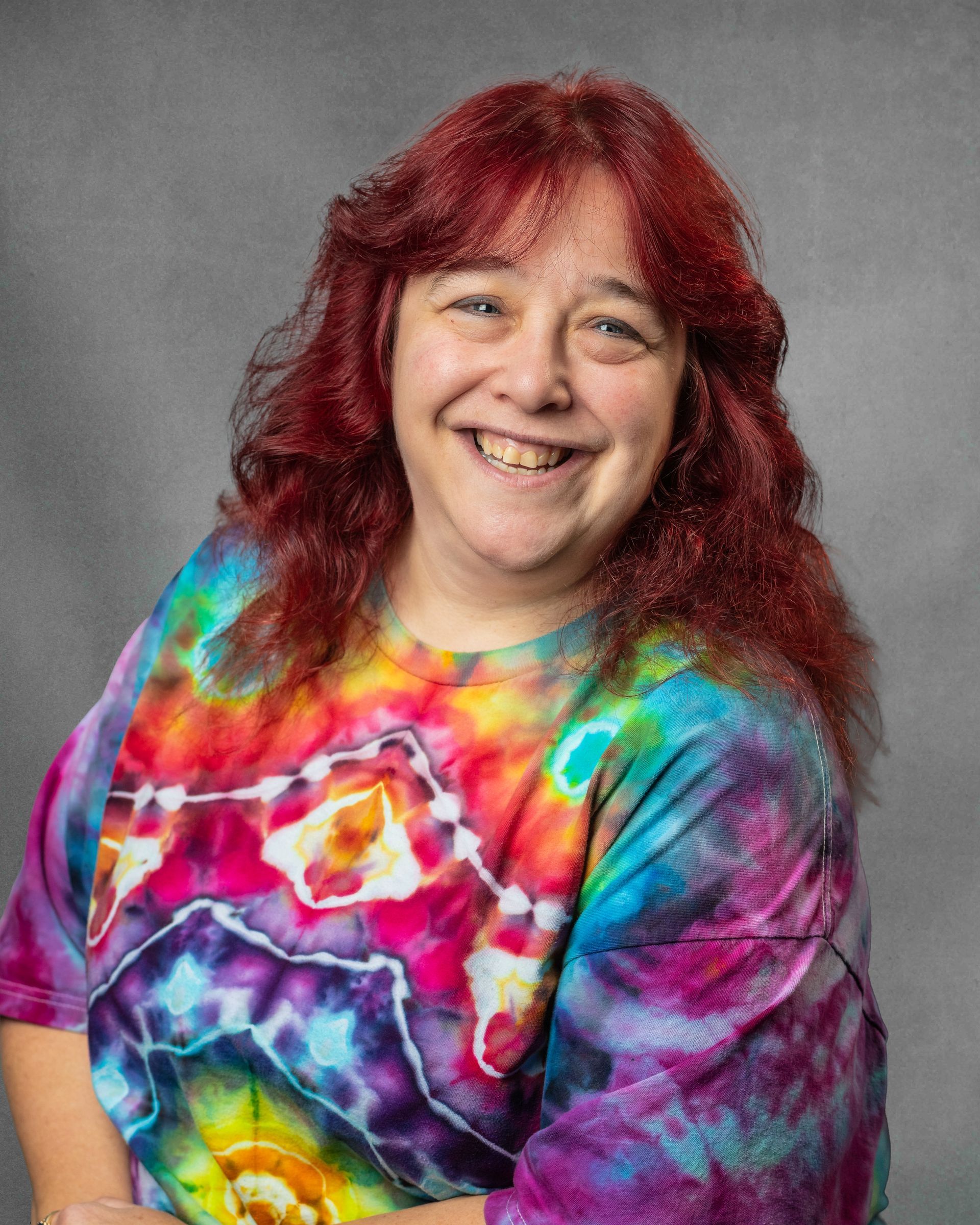 A woman in a tie dye shirt is smiling at the camera.