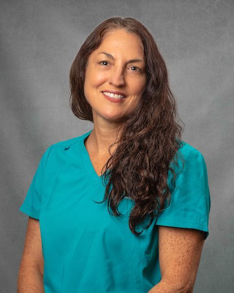 A woman in blue scrubs is smiling.
