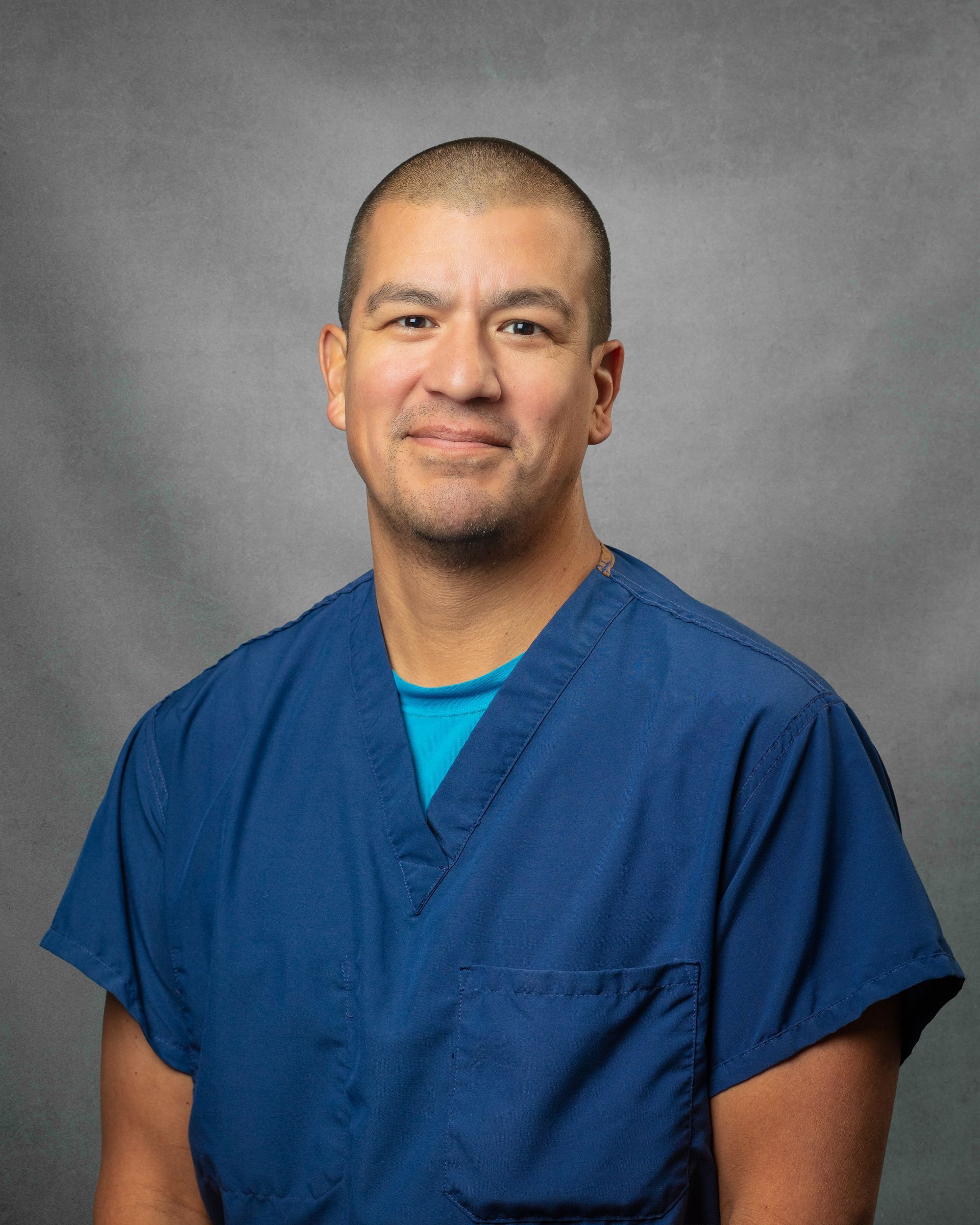 A man wearing blue scrubs is smiling for the camera.
