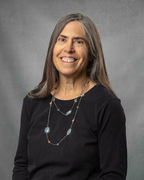 A woman wearing a black shirt and a long necklace is smiling for the camera.