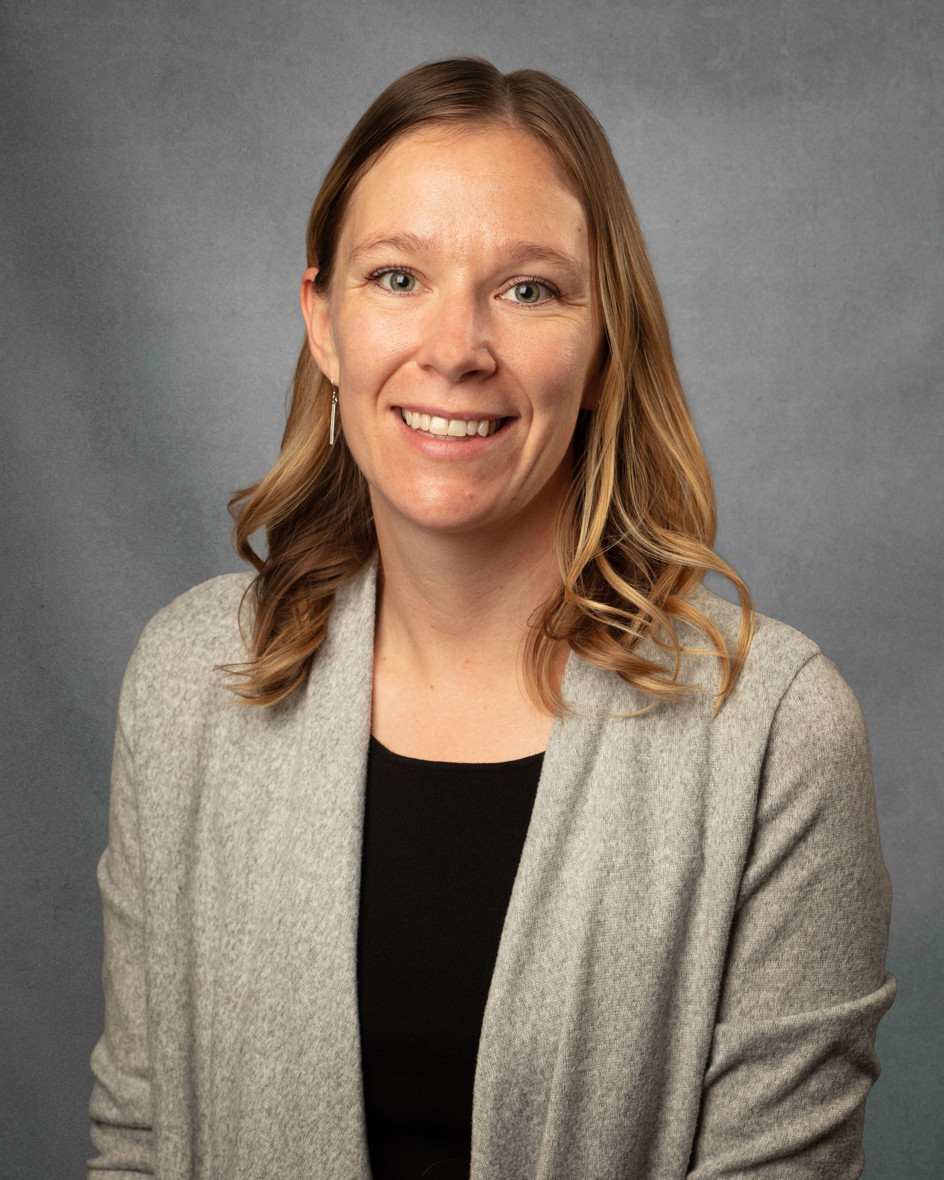 A woman in a gray cardigan is smiling.