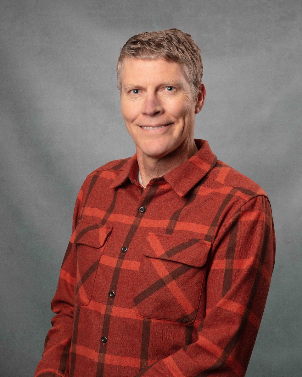 A man wearing an orange plaid shirt is smiling for the camera