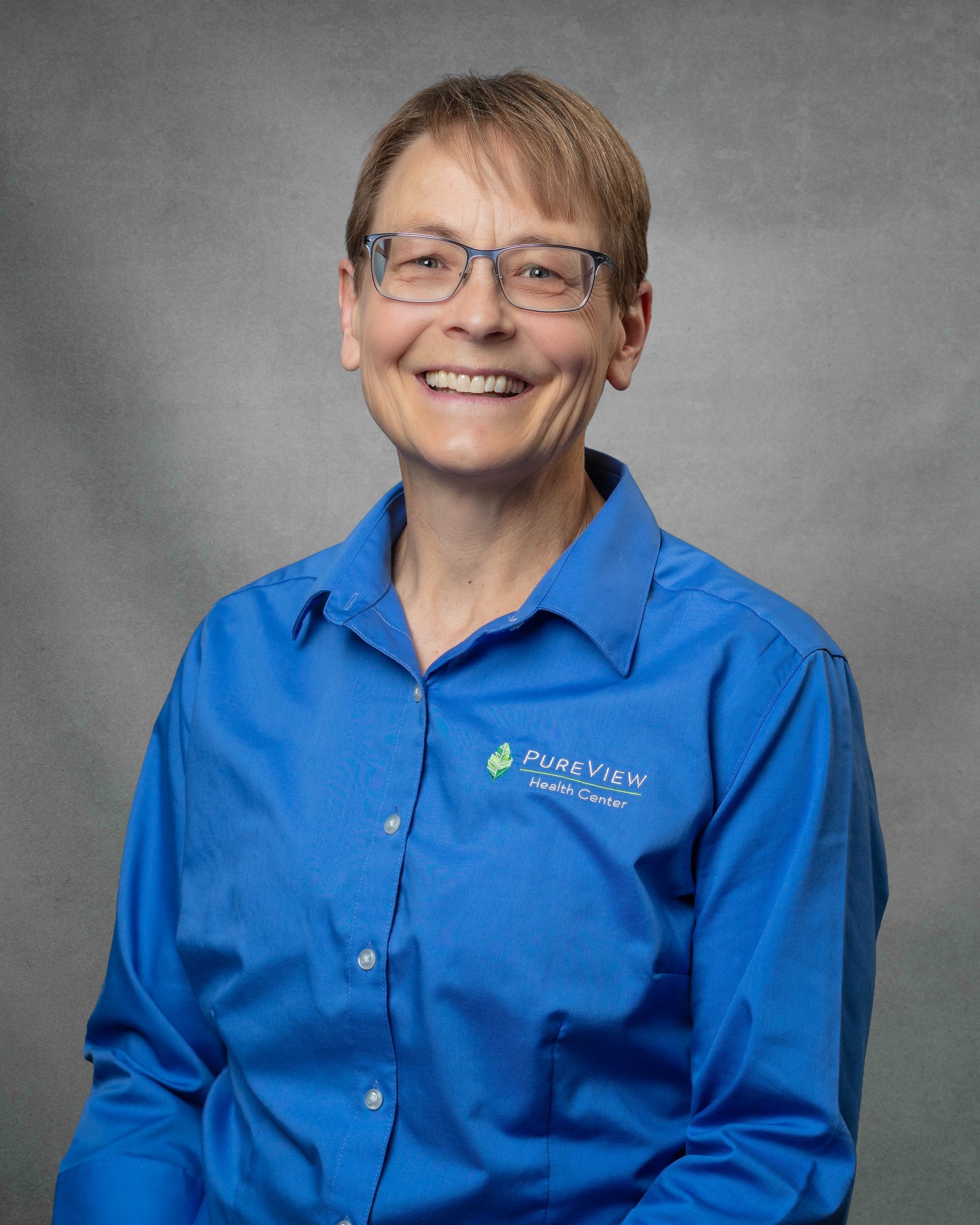 Joelle Selk. A woman wearing glasses and a blue shirt is smiling for the camera.