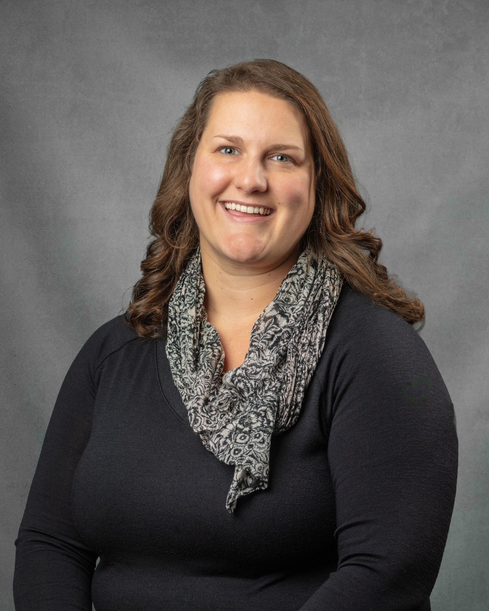 A woman in a black shirt and a patterned scarf is smiling for the camera.