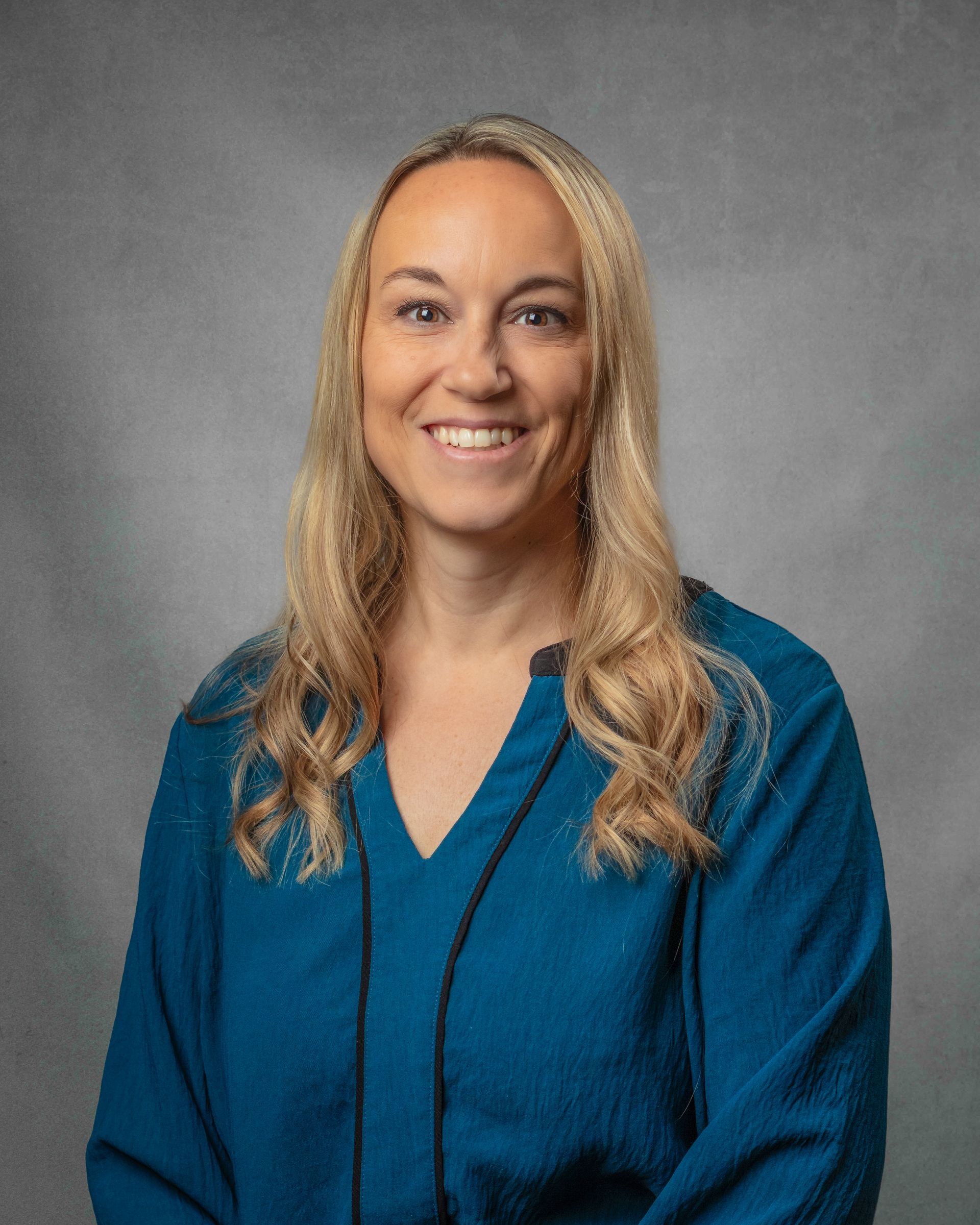 A woman with long blonde hair is wearing a blue shirt and smiling for the camera.