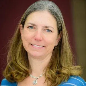 A woman wearing a blue striped shirt and a necklace is smiling for the camera.