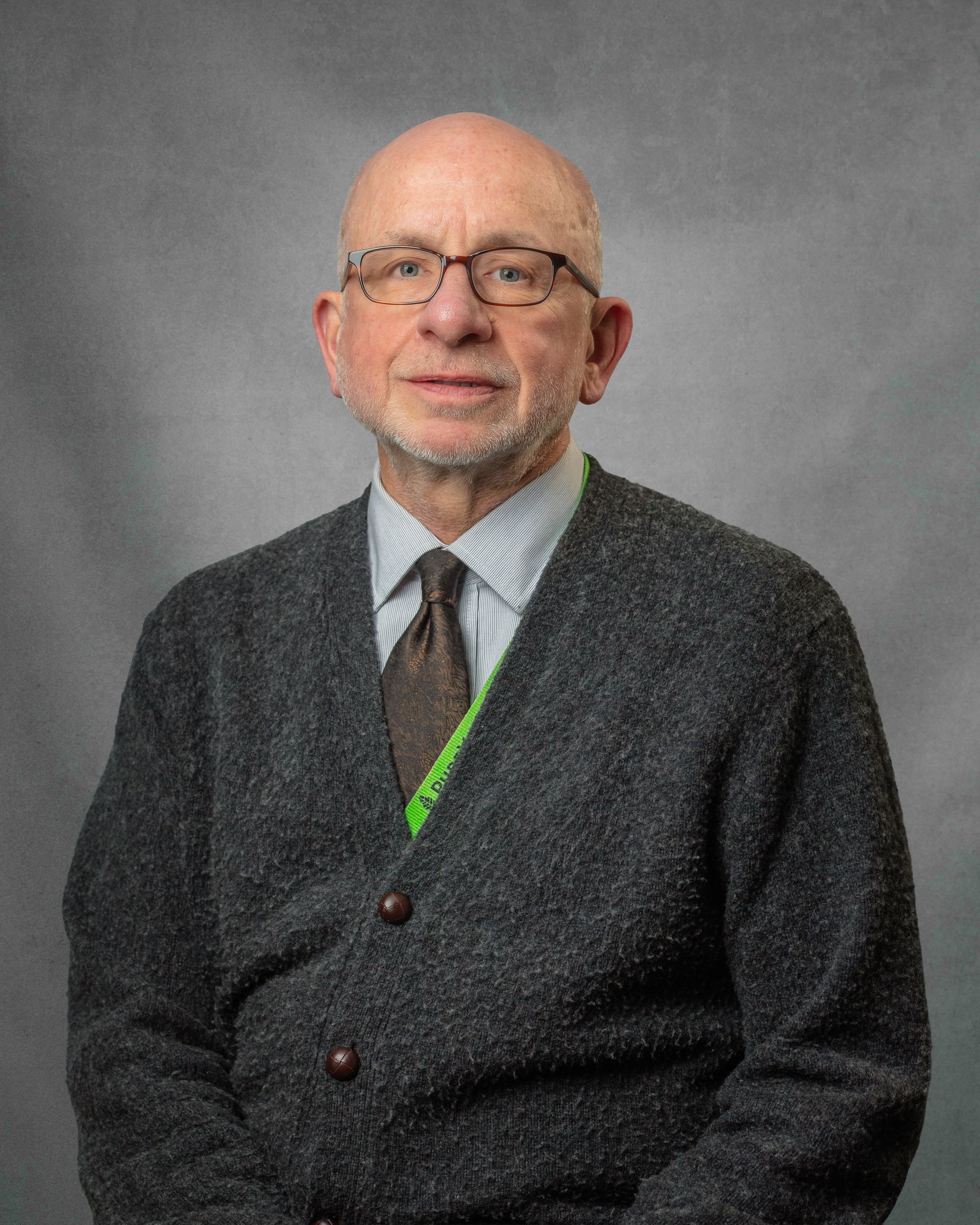 A man wearing glasses and a gray cardigan with a tie is posed for the camera.