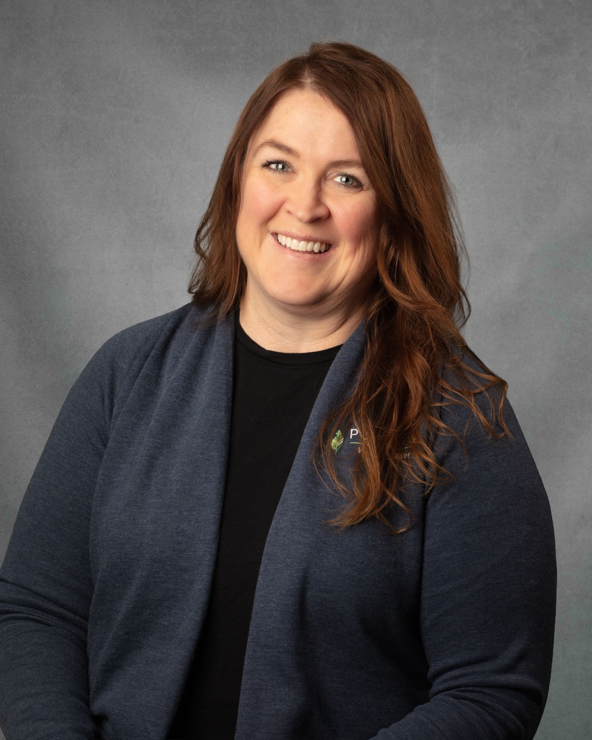 A woman with long brown hair in a gray cardigan is smiling for the camera.