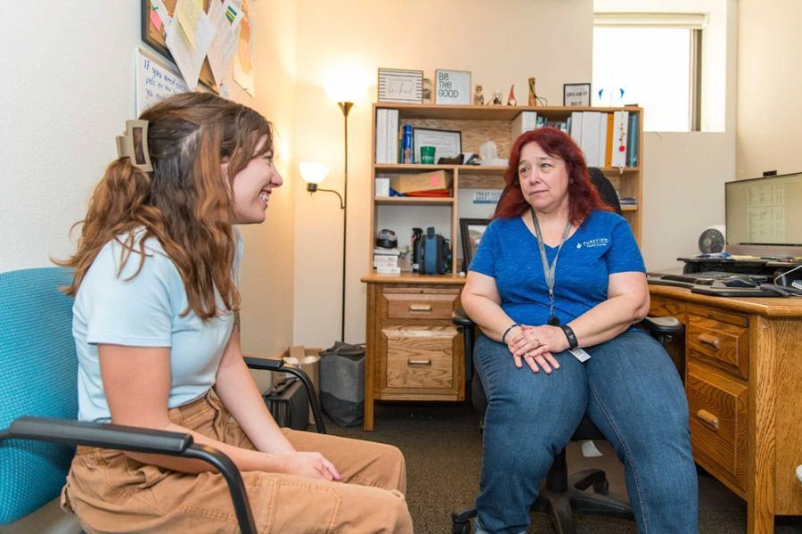 Two women are sitting in chairs in a room talking to each other.