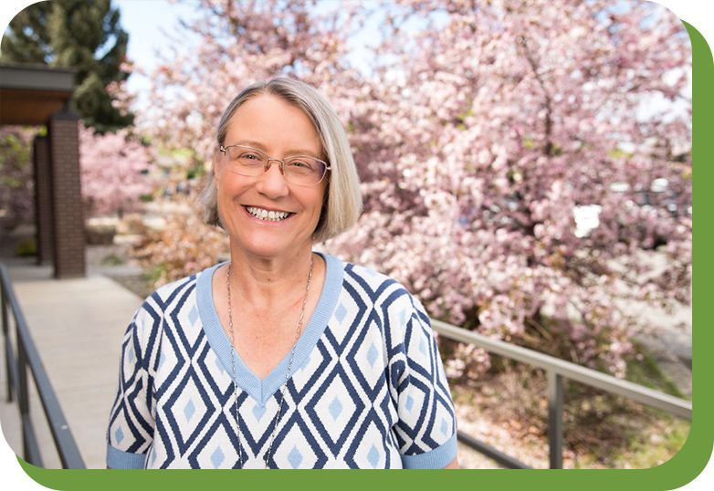 A woman is smiling in front of cherry blossoms.