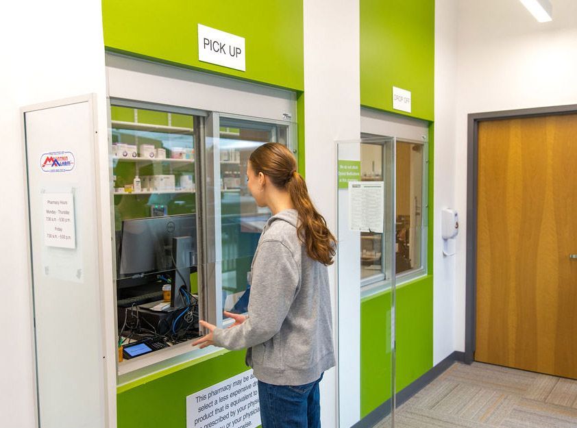 A woman is picking up a prescription at a pharmacy window.