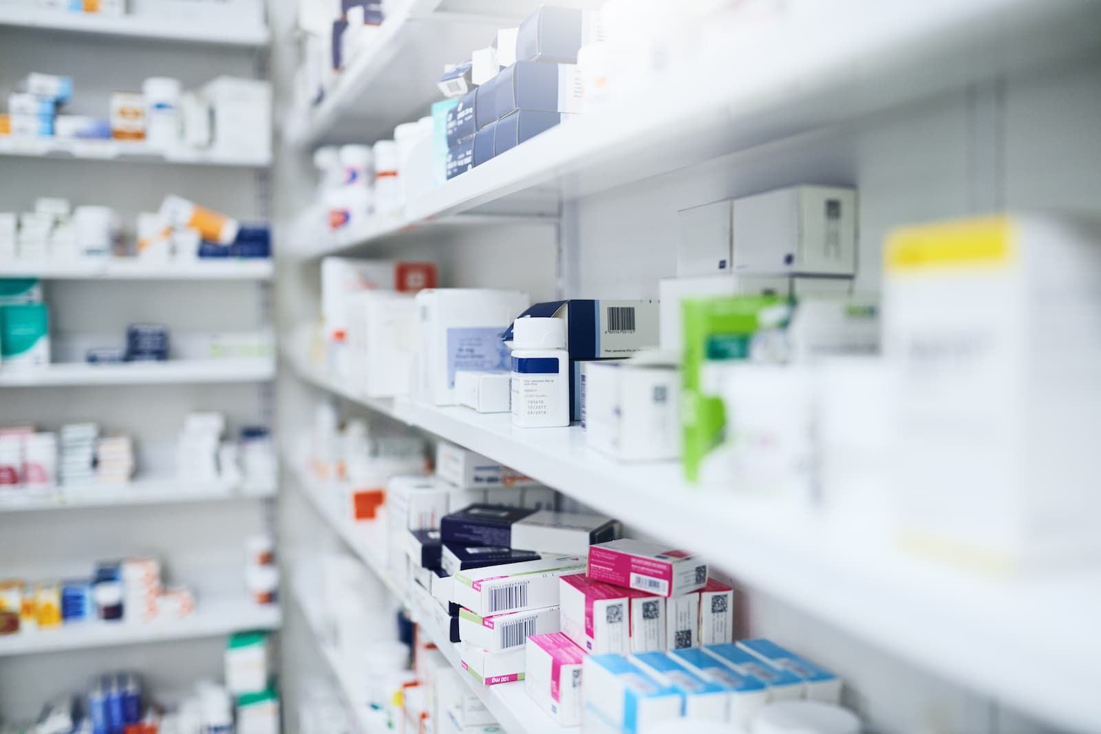 Pharmacy shelves stocked with various boxes and containers of prescription medications and OTC meds.