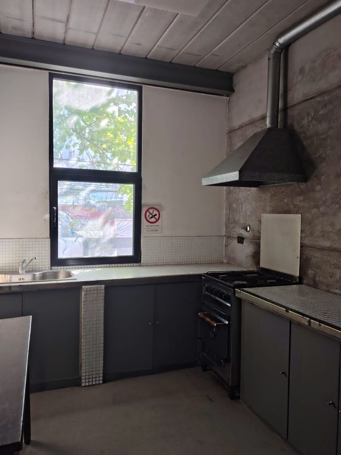 Cocina pequeña con armarios oscuros, paredes de azulejos blancos, ventana, fregadero, estufa y campana extractora negra.