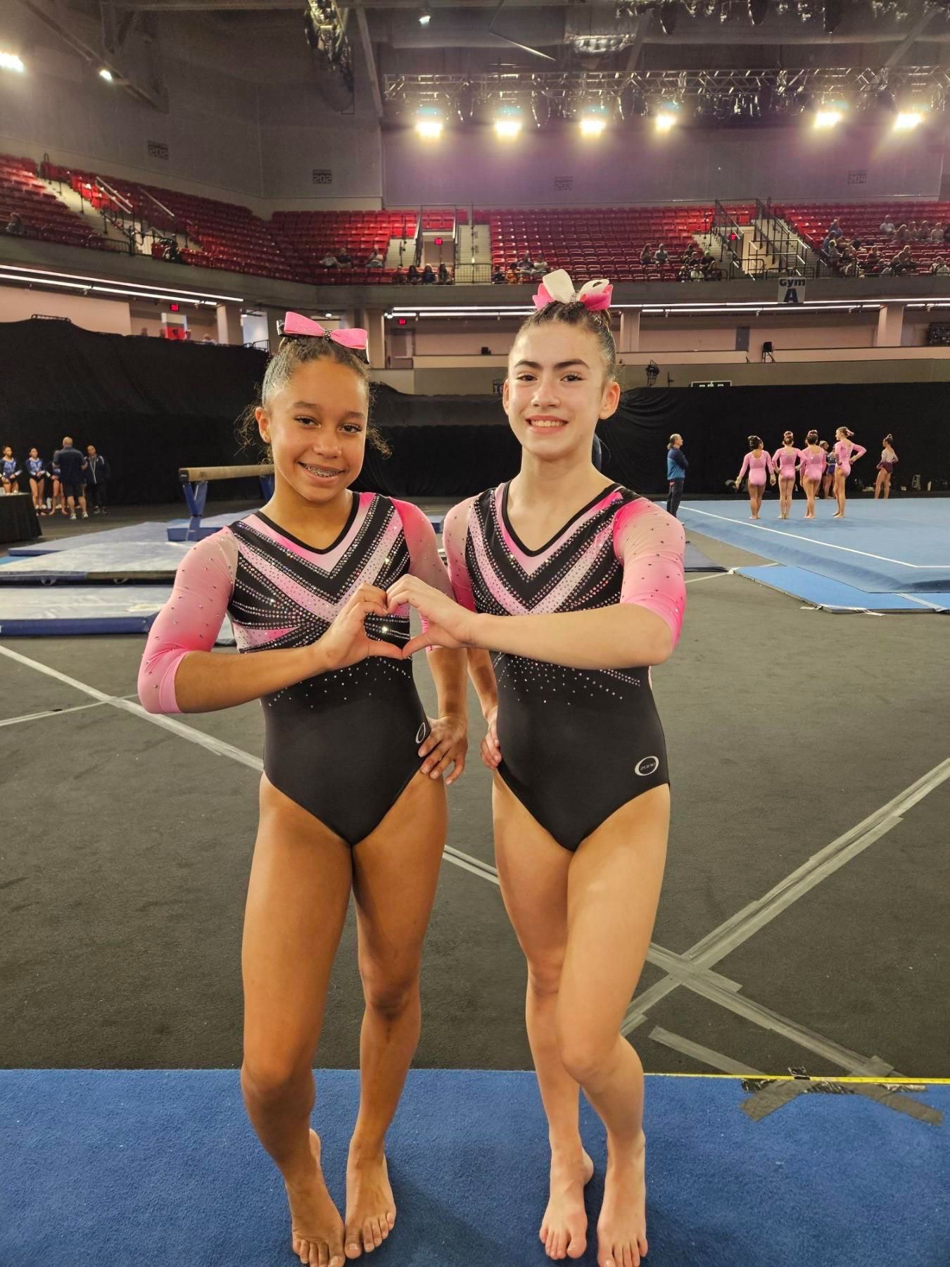 Two gymnasts in matching leotards posing together at a gymnastics meet