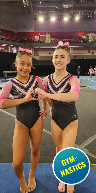 Two young gymnasts in sparkly leotards making a heart shape with their hands