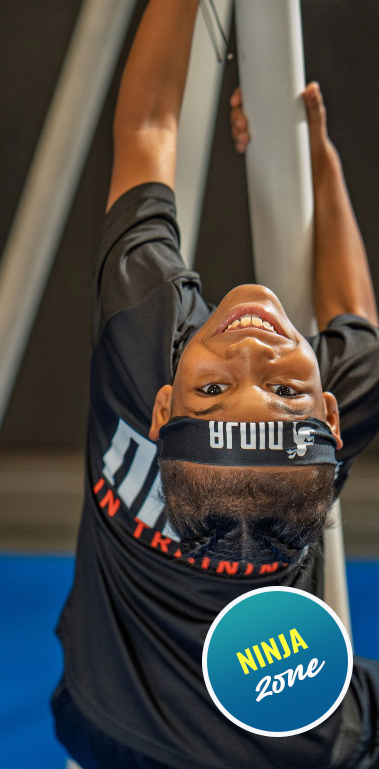 Smiling boy hanging upside down during a Ninja Zone class