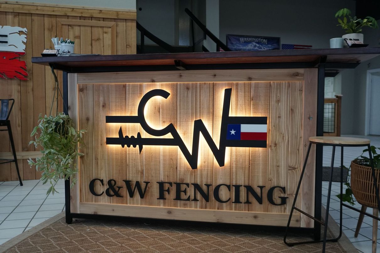 C&W FENCING illuminated sign on a wooden reception counter, with a Texas flag emblem and rustic decor