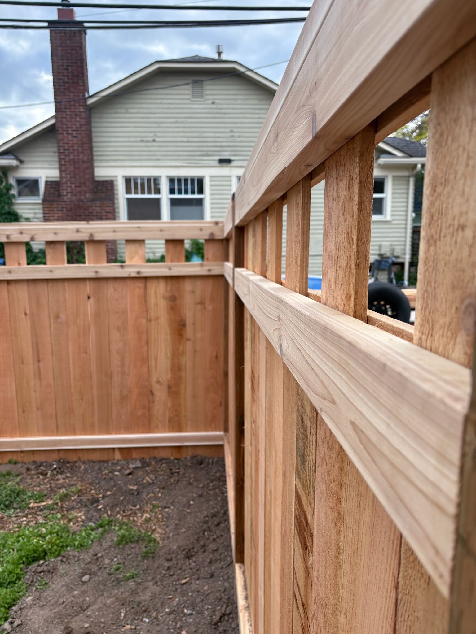 Wooden fence under construction in a backyard, with vertical posts, horizontal rails, and a house in the background