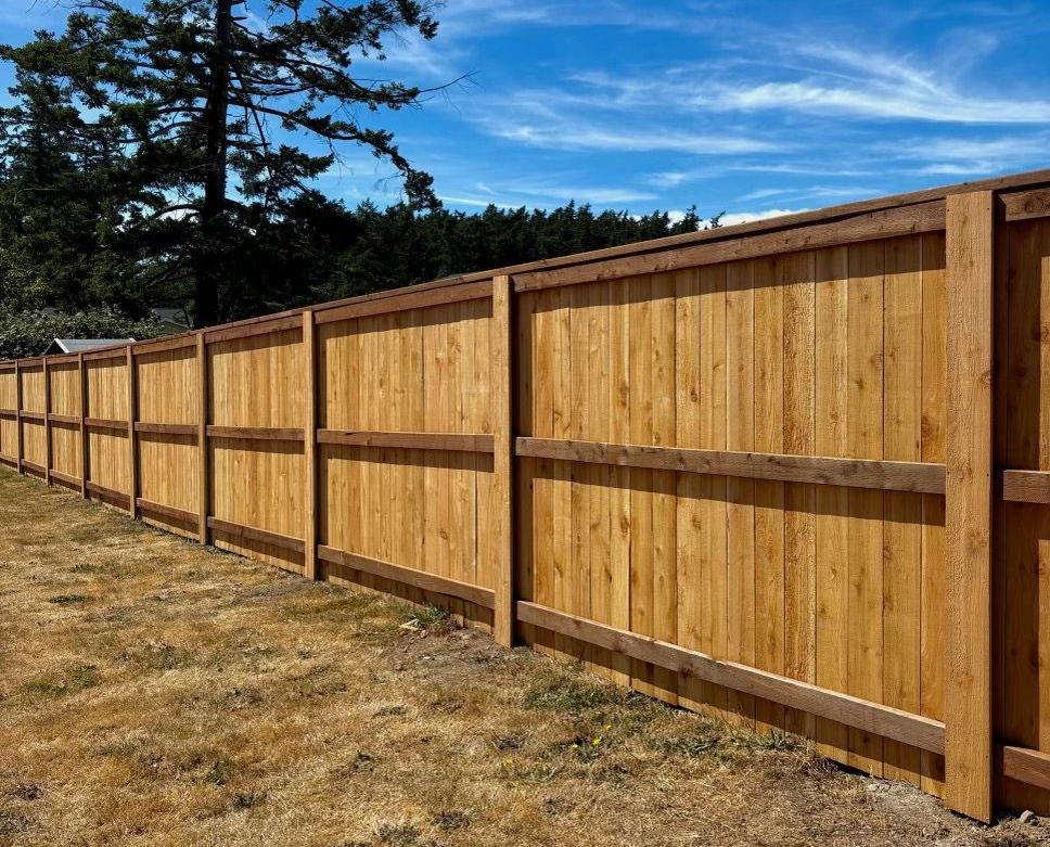 Wooden privacy fence with brown posts and rails along a dry grassy yard under a blue sky