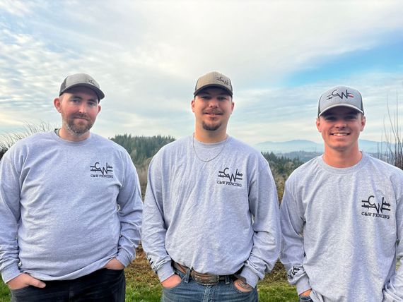 Three men in gray sweatshirts and caps standing outdoors under a cloudy sky